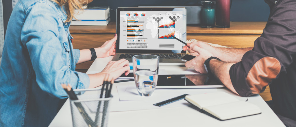 Businessman and businesswoman sitting at table in front of laptop and working. Graphs,charts and diagrams on PC screen.